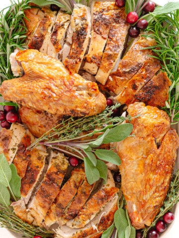 Carved dry brined spatchcock turkey with herb butter on a platter garnished with herbs and cranberries.