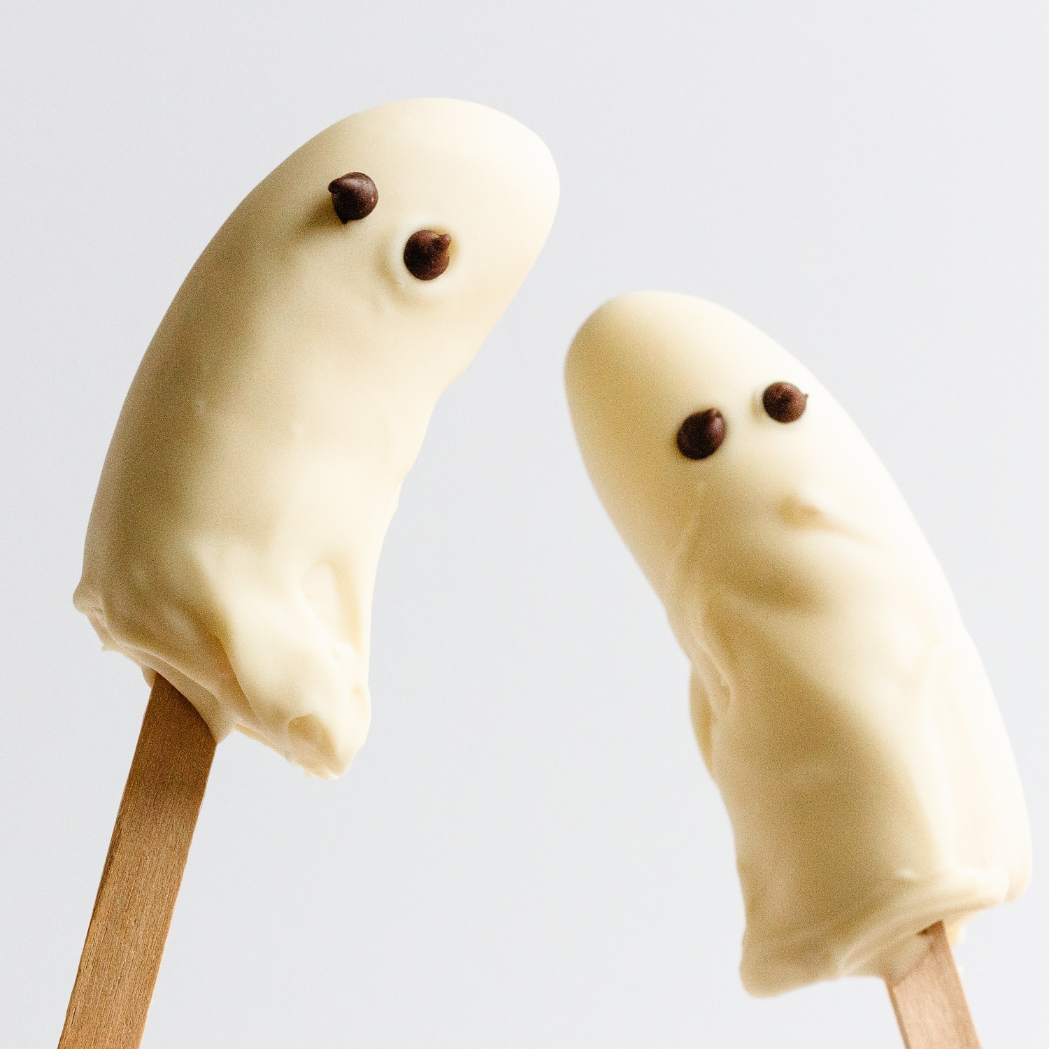 Two frozen ghost bananas covered in white chocolate with chocolate chip eyes.