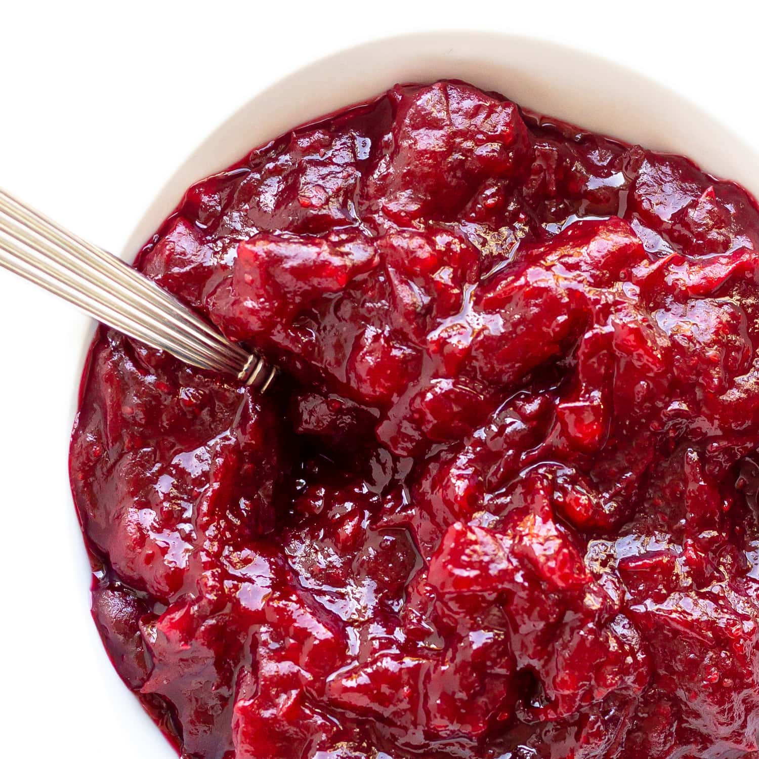 Homemade cranberry sauce in a white bowl with spoon.
