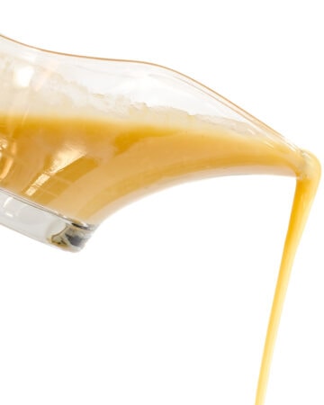Turkey gravy pouring out of a glass gravy boat against a white background.
