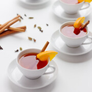 White tea cups on saucers filled with orange spiced mulled tea and garnished with an orange slice and cinnamon stick.