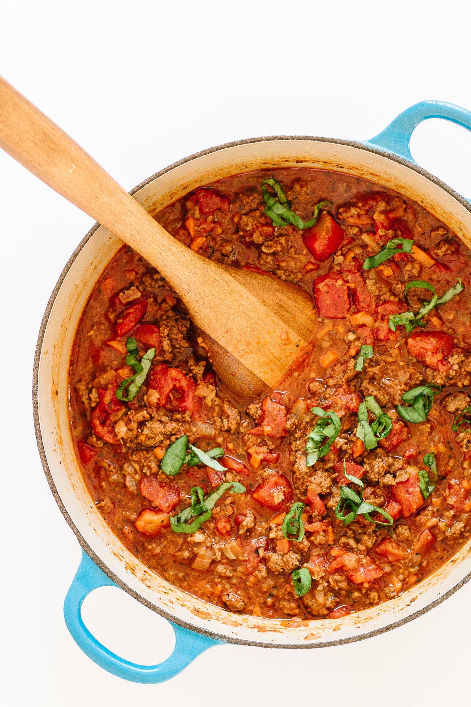 Bolognese sauce in a dutch oven with blue handles and a wooden spoon sticking out