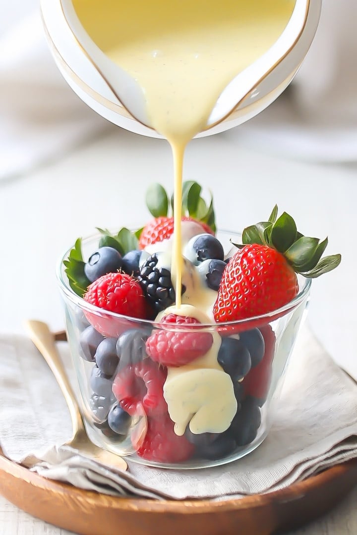 Creme anglaise being poured onto a bowl of mixed berries.