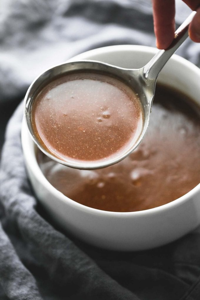 Beef Gravy being lifted with a stainless steel ladle out of a white bowl