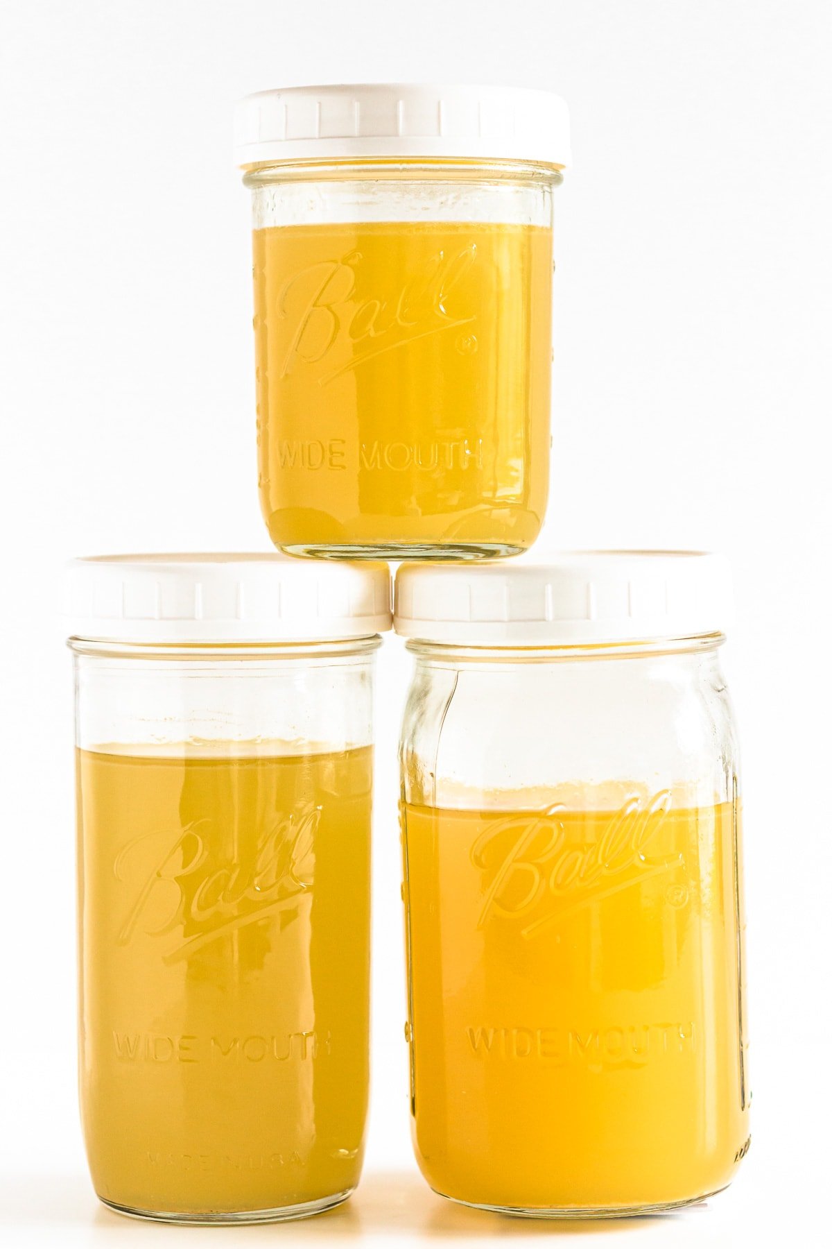 Three stacked up mason jars filled with turkey stock on a white background.