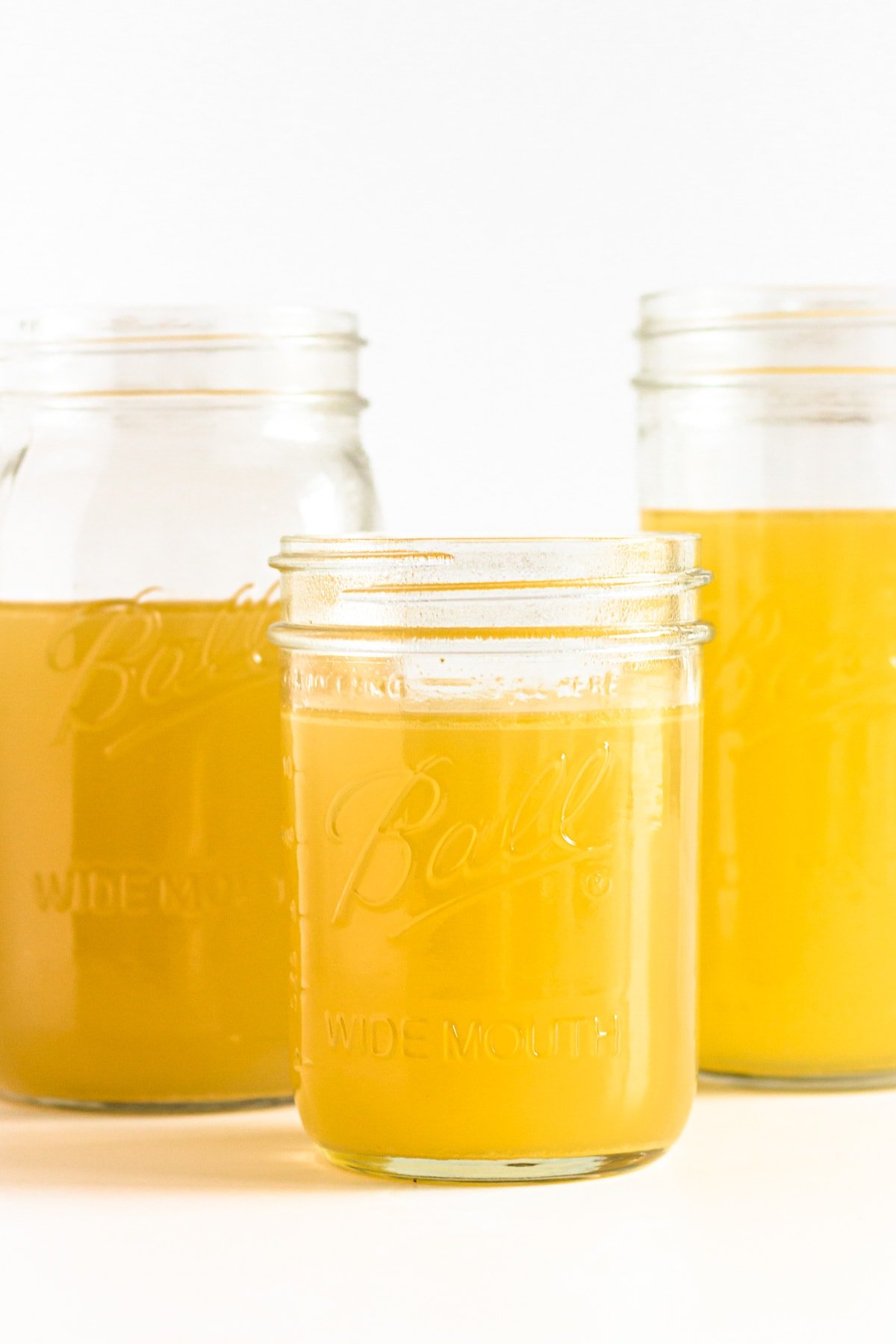 Three mason jars of turkey bone broth on a white background.