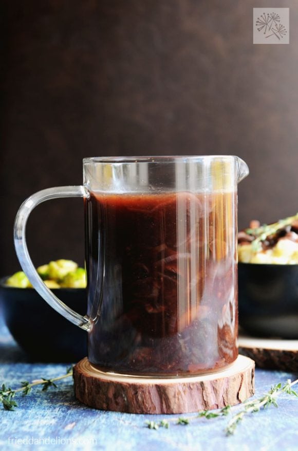 Vegan red wine gravy in a clear glass gravy pitcher set on a round wood slice