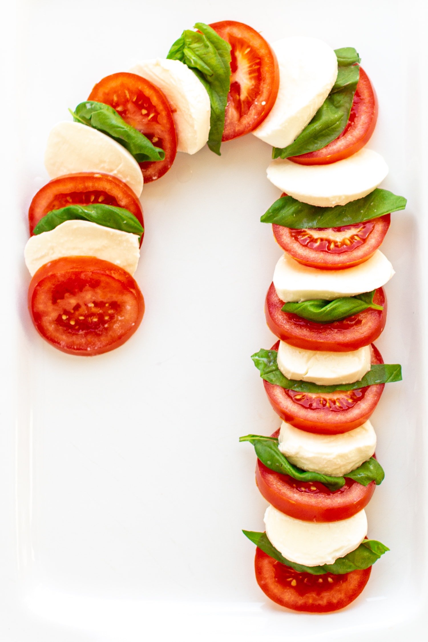 Caprese salad arranged in the shape of a candy cane on a white platter.