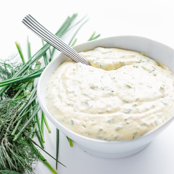 White bowl of creamy herb sauce with fresh herbs beside it.