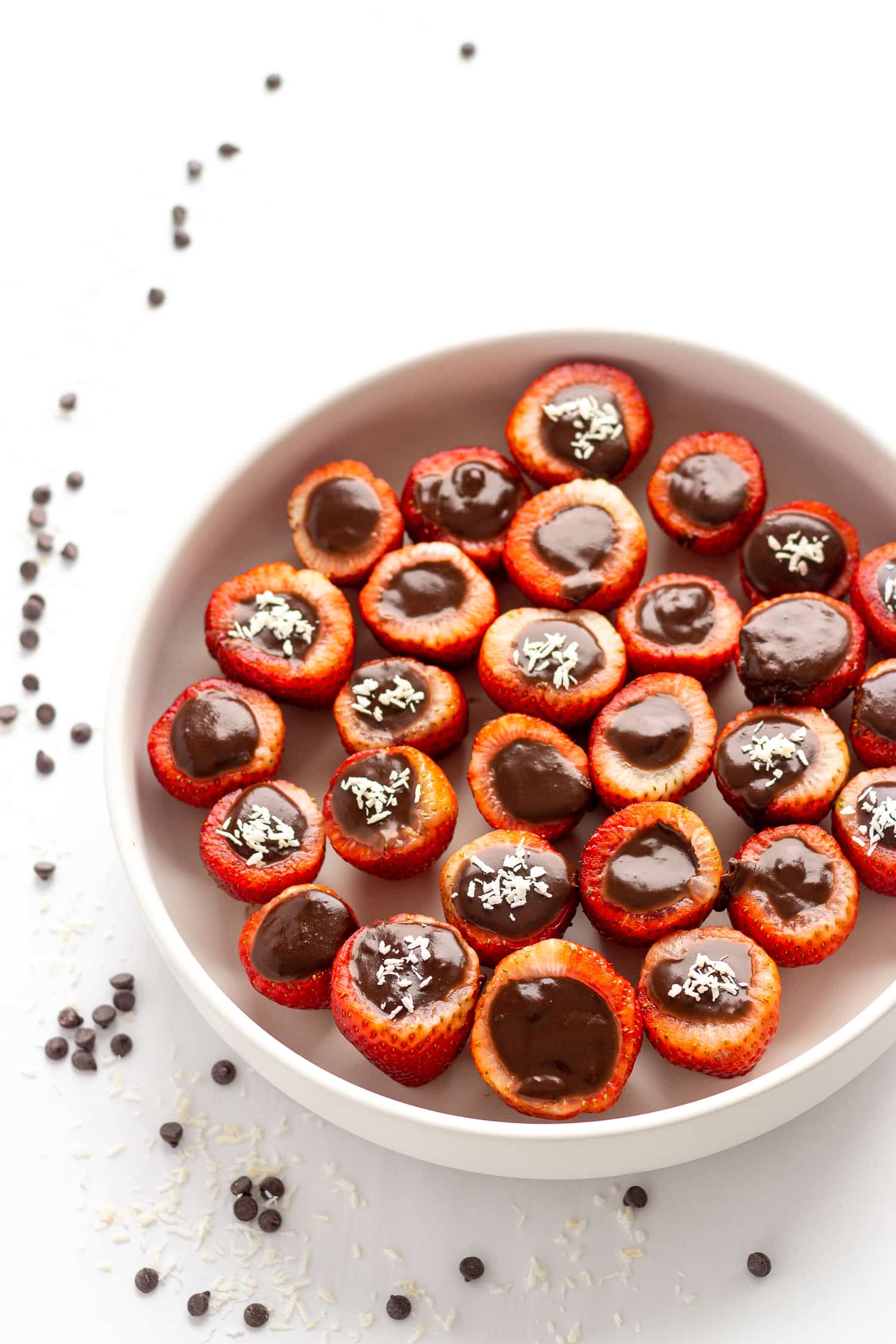 White bowl filled with chocolate coconut cream stuffed strawberries.  Set on a white background with a scattering of chocolate chips and shredded coconut.