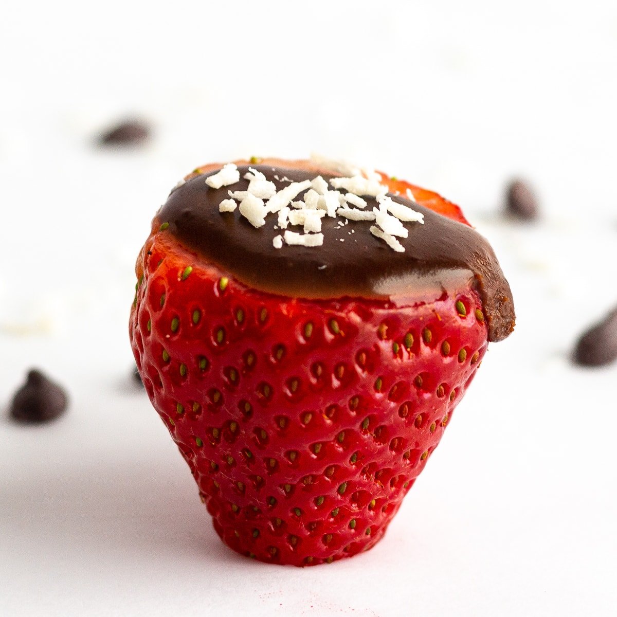 Single strawberry filled with chocolate coconut cream and a few flakes of shredded coconut scattered on the top.