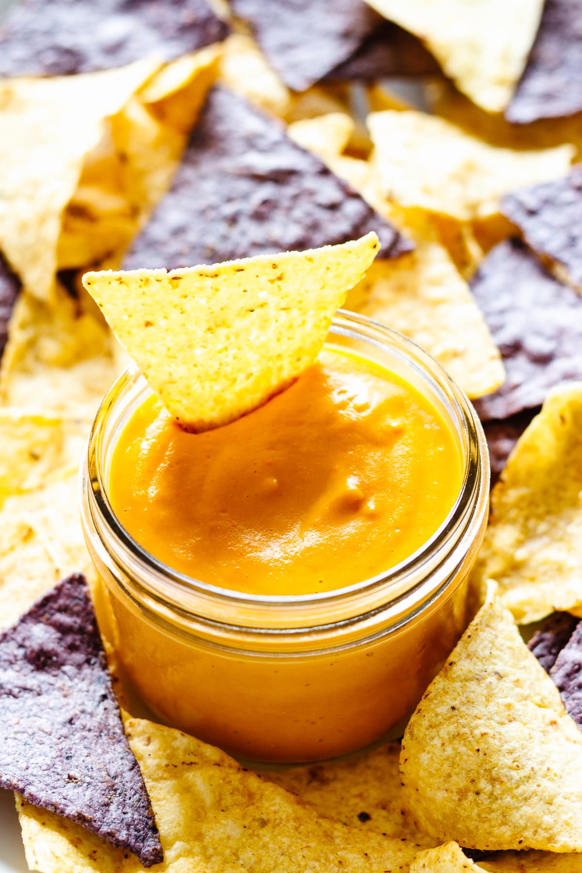 Mason jar filled with vegan nacho cheese sauce and surrounded by yellow and blue corn tortilla chips