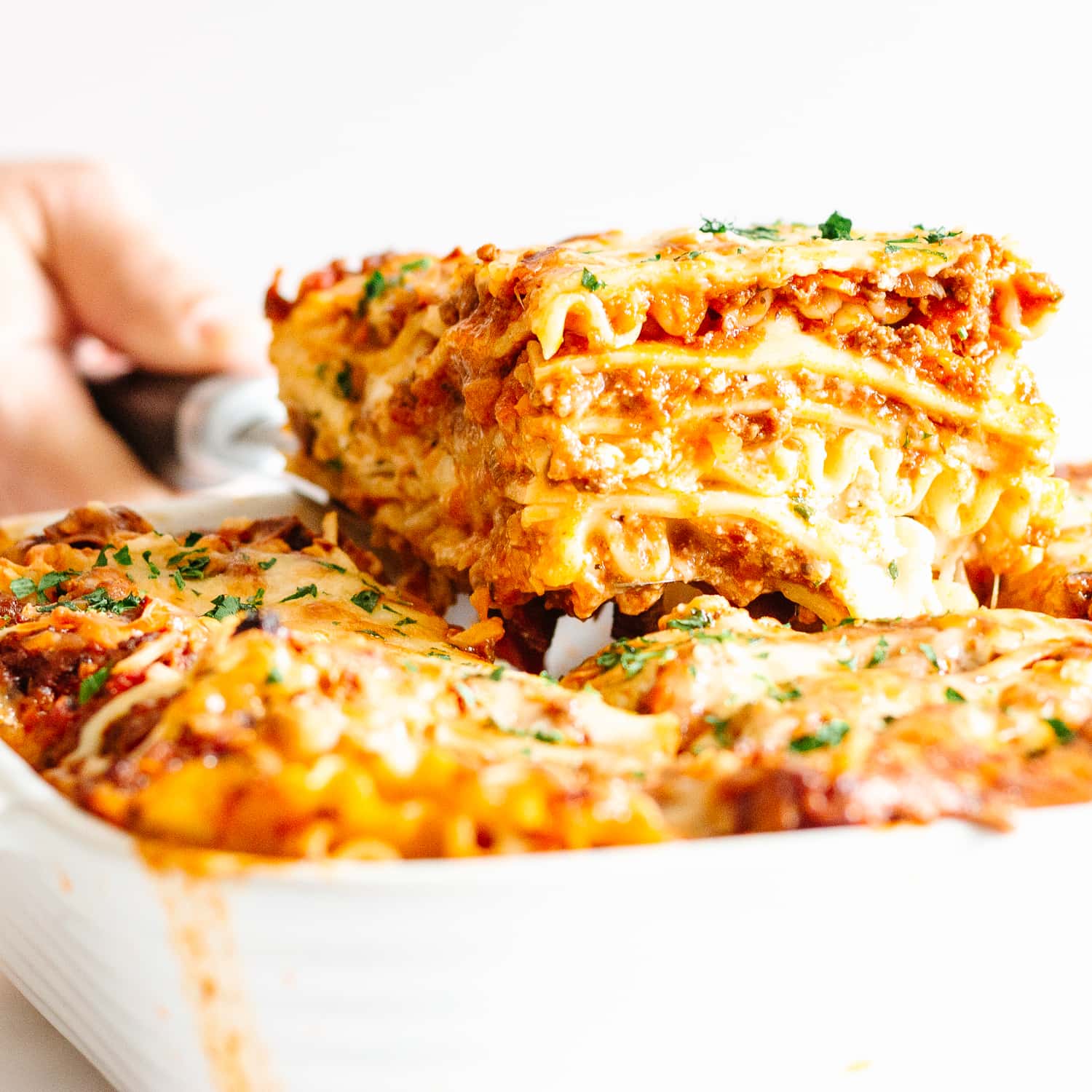 Slice of lasagna being lifted out of casserole dish.