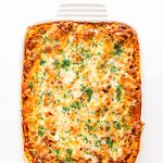 Overhead shot of lasagna in a white dish on a white background