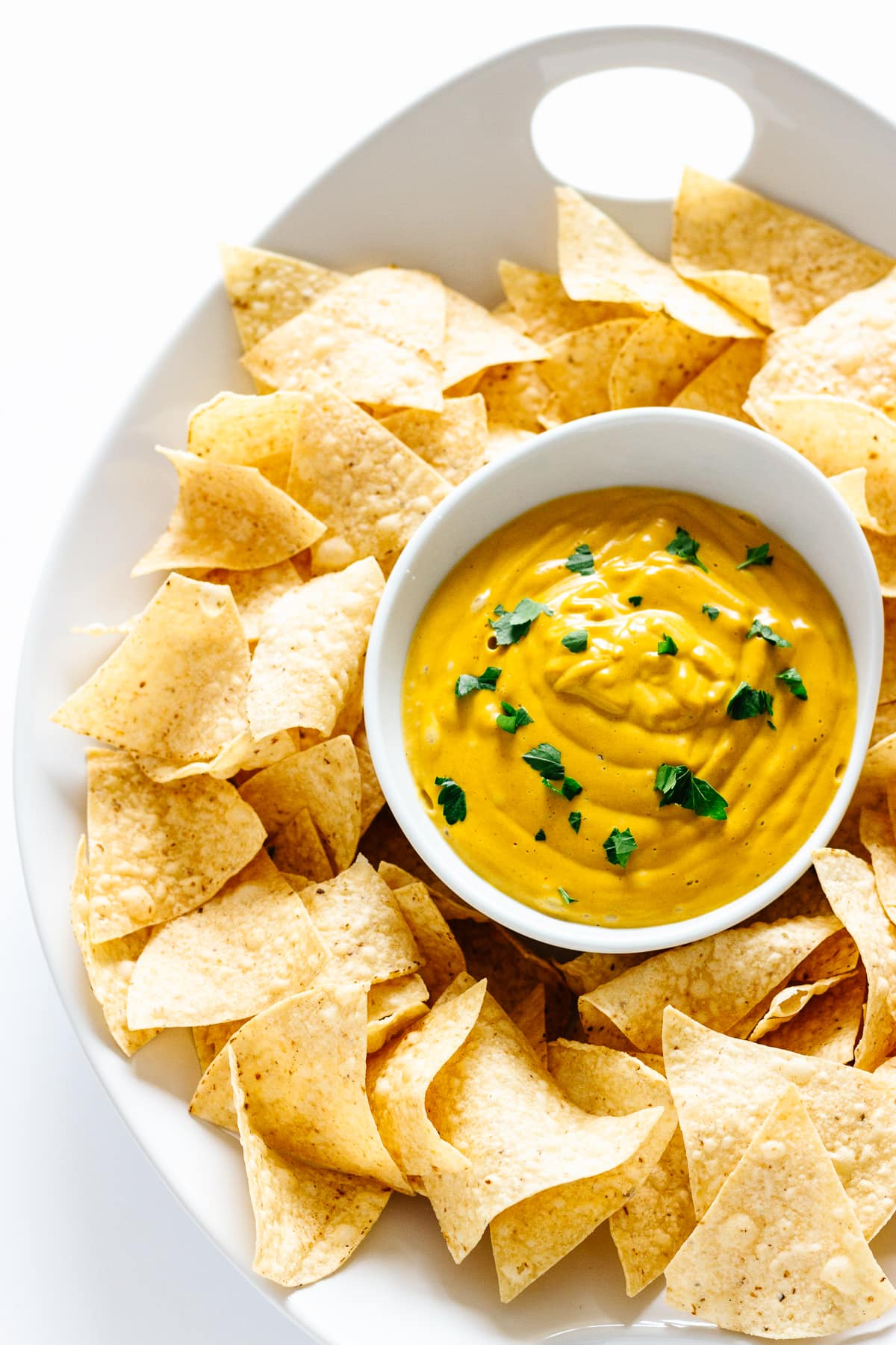 White platter of tortilla chips with bowl of nacho queso dip in the center.