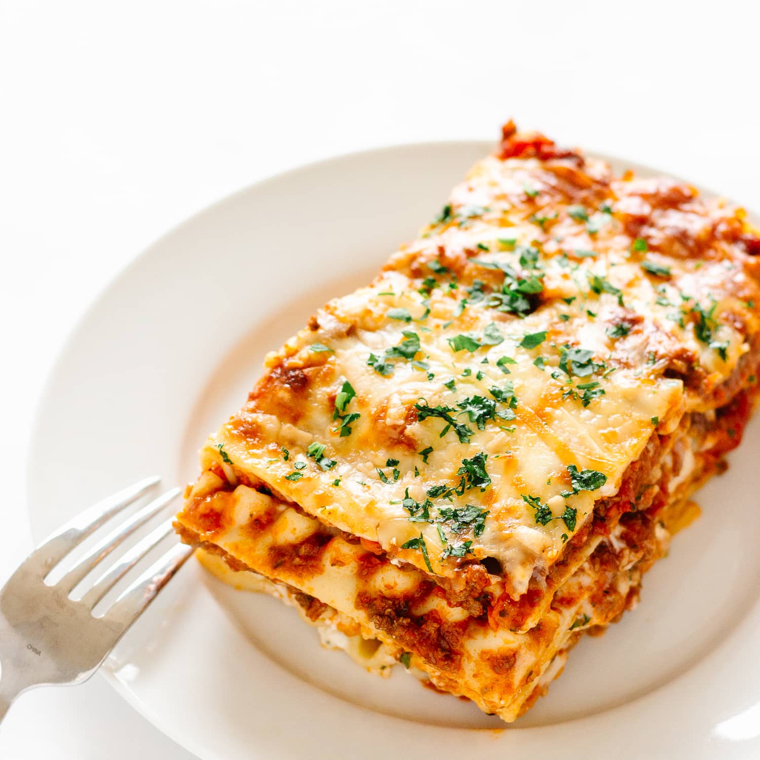 Slice of lasagna on a white plate with fork resting on the side.