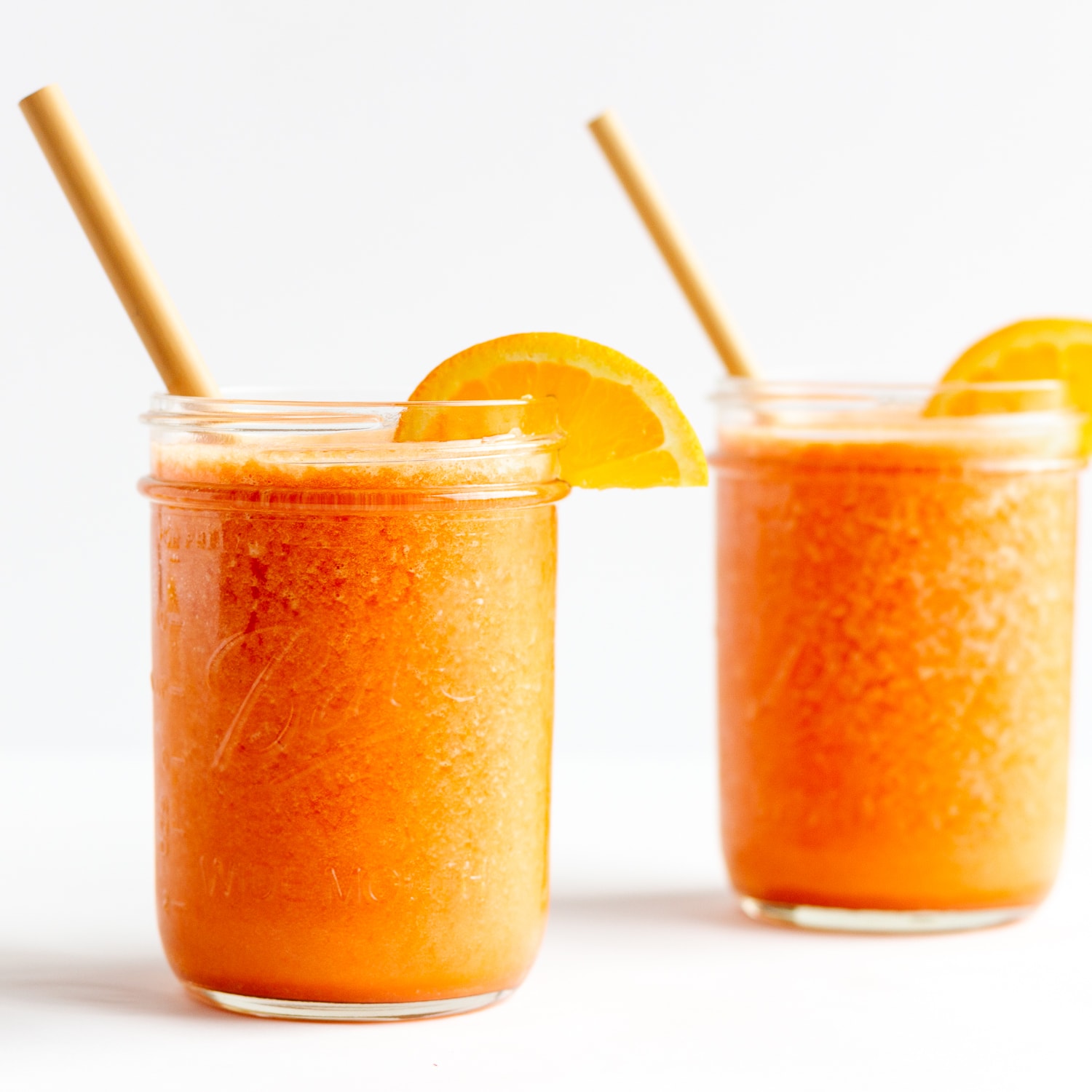 Two mason jars filled with Vitamin C Immune Boosting Smoothie and garnished with orange slices and a bamboo straw.