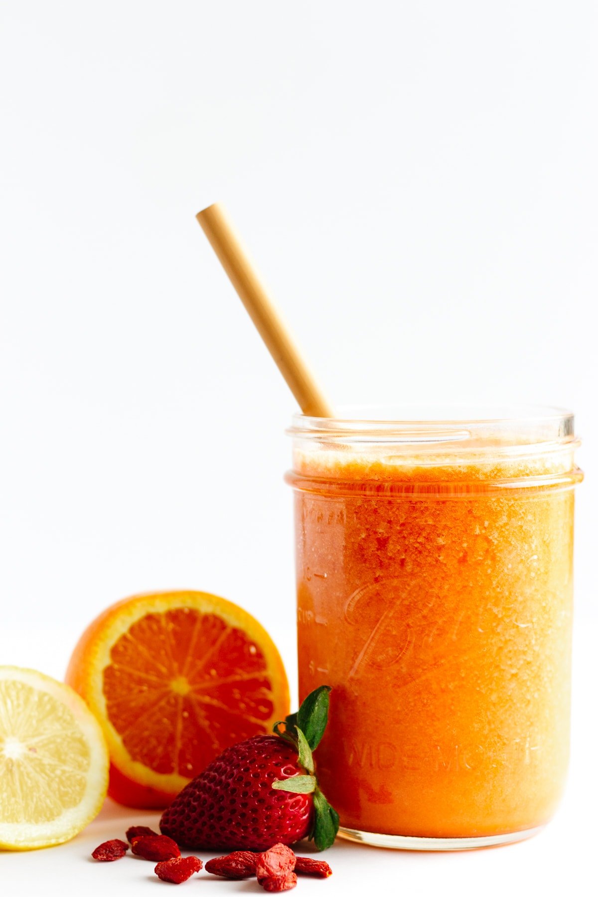 Smoothie in mason jar with bamboo straw with fruit sitting next to it.