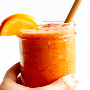 Hand holding a vitamin c powerhouse smoothie in a glass jar with bamboo straw and orange slice garnish.