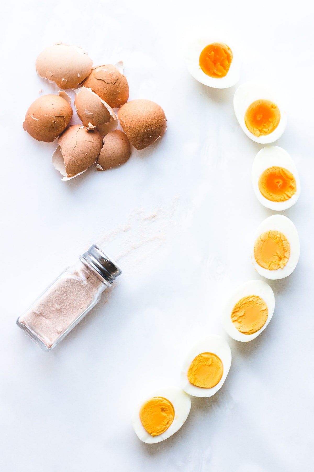 Hard boiled eggs sliced in half with pile of shells and salt shaker on the side.