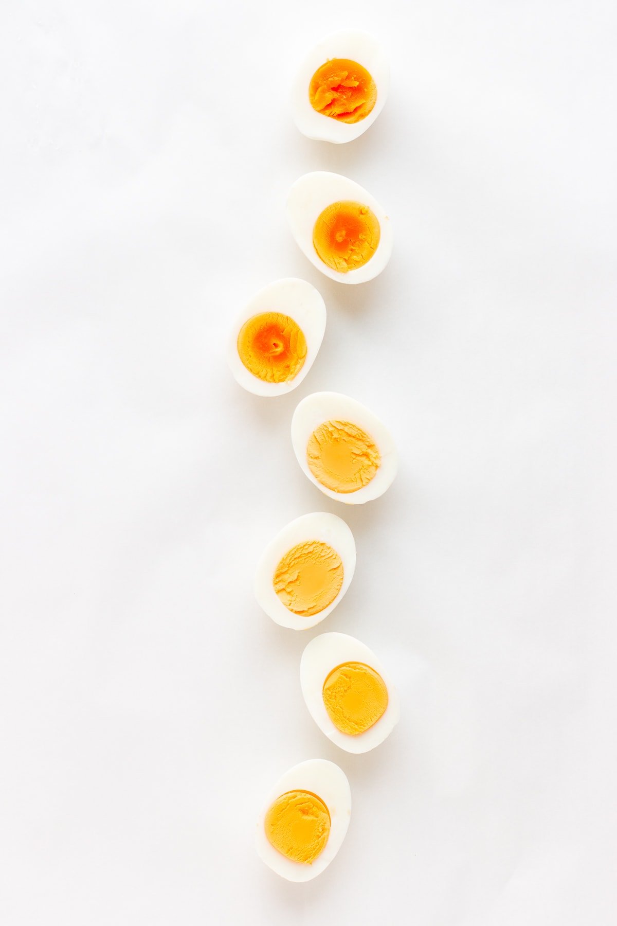 Vertical line of halved hard boiled eggs on a white background.