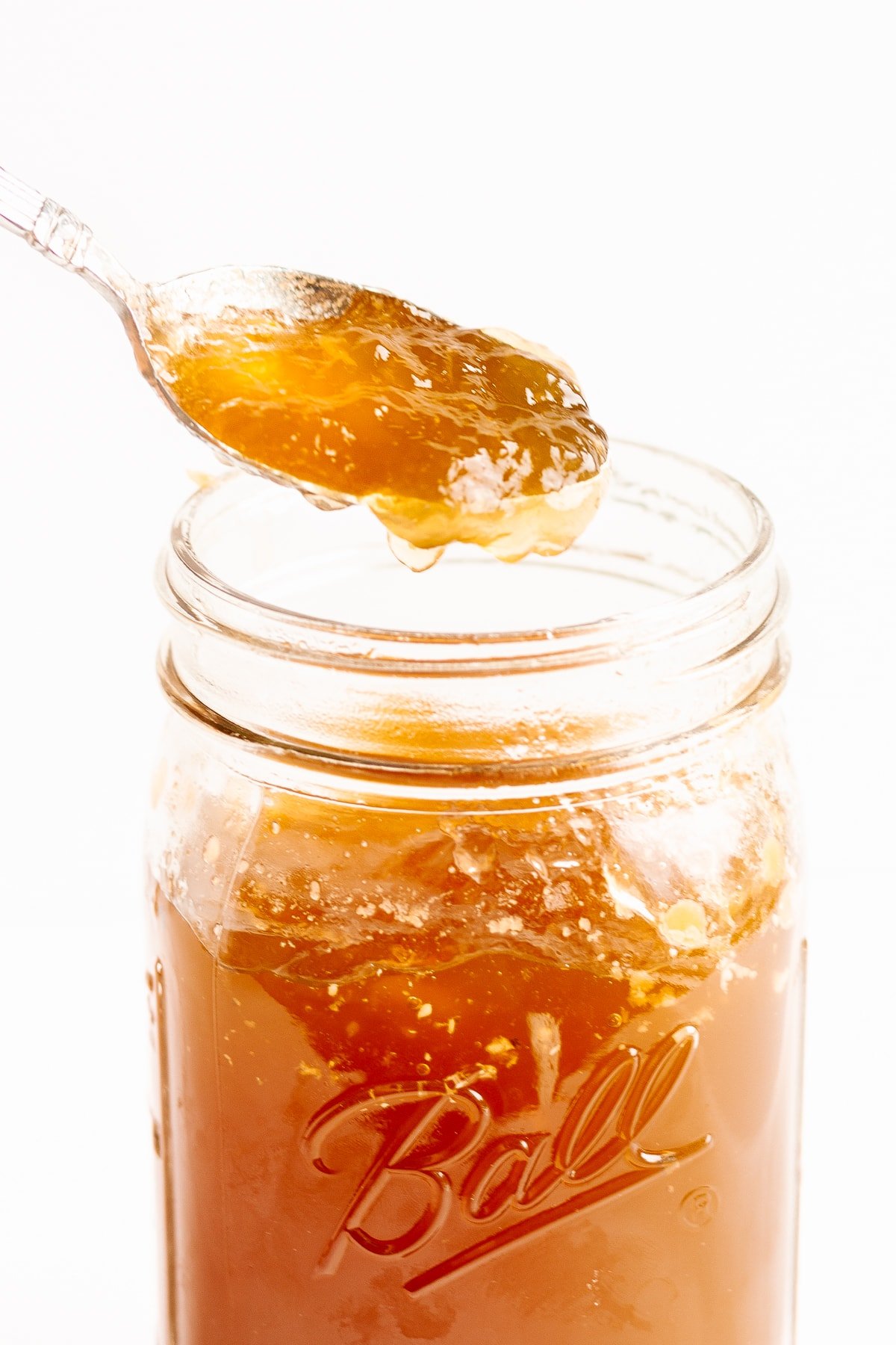 Chilled bone broth lifted out of a glass mason jar on a spoon.