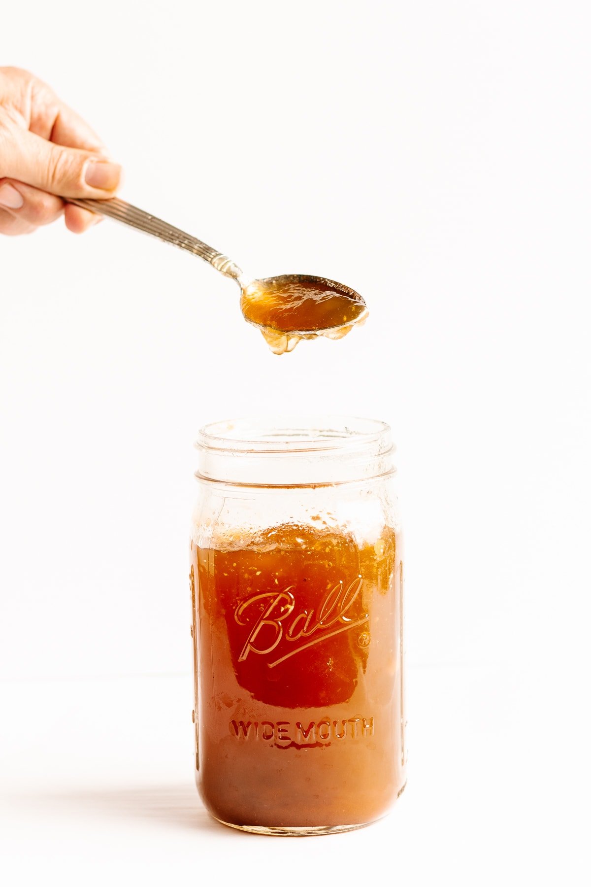 Hand holding spoon scooping out some chilled beef bone broth from a mason jar.