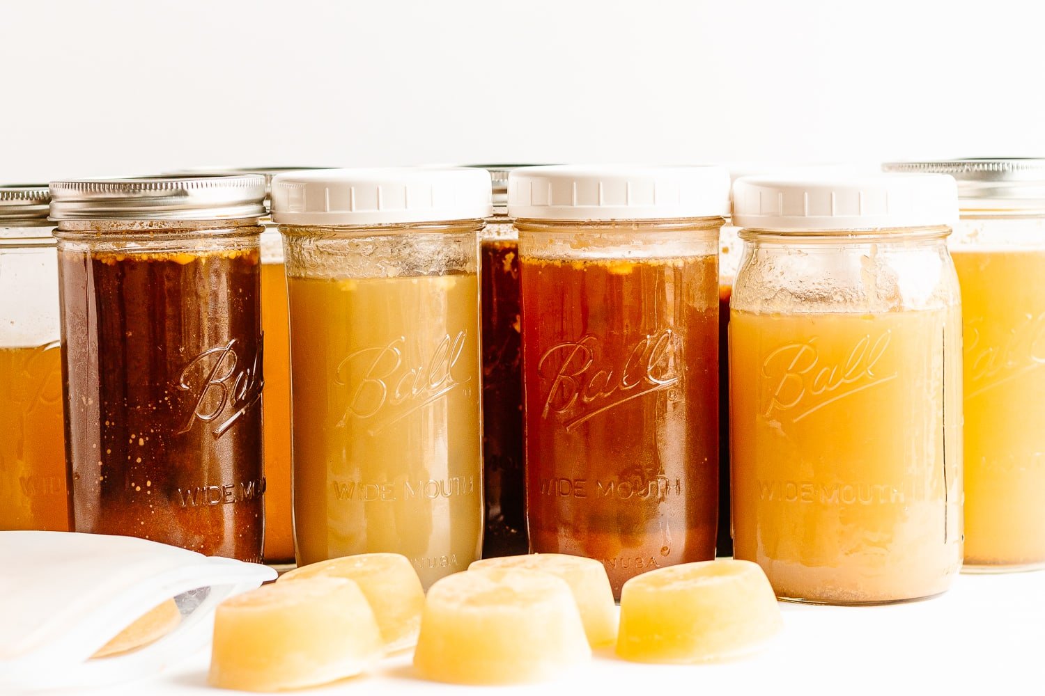 A variety of mason jars filled with broths and stocks with some frozen broth "pucks" in front.