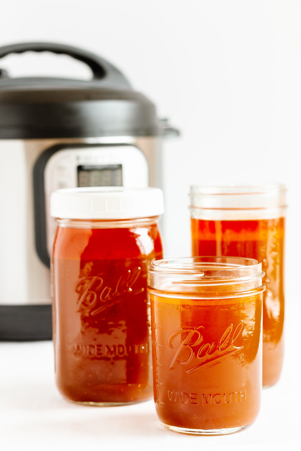 Three mason jars of beef bone broth with Instant Pot in the background.