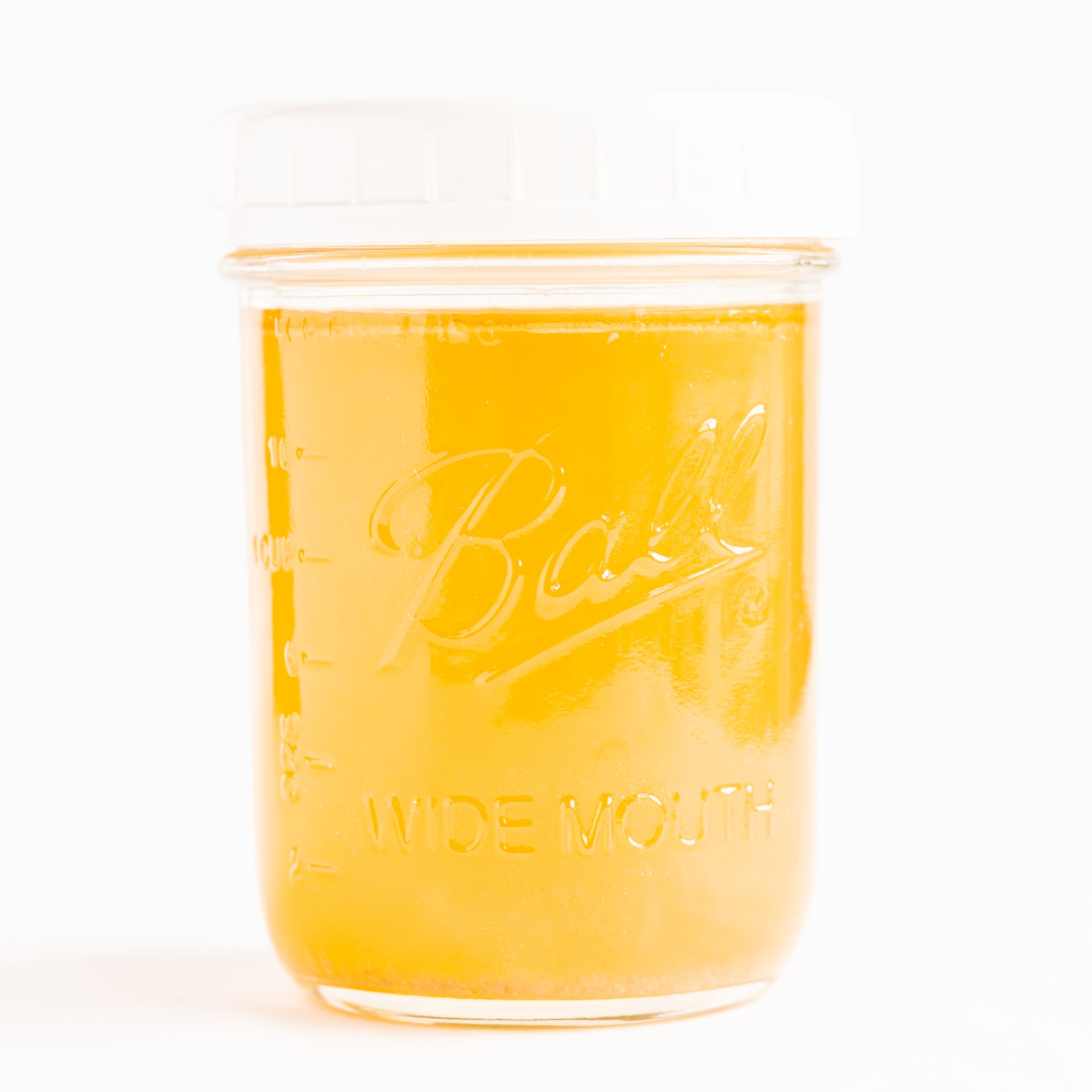 Mason jar of chicken stock with white plastic lid on a white background.