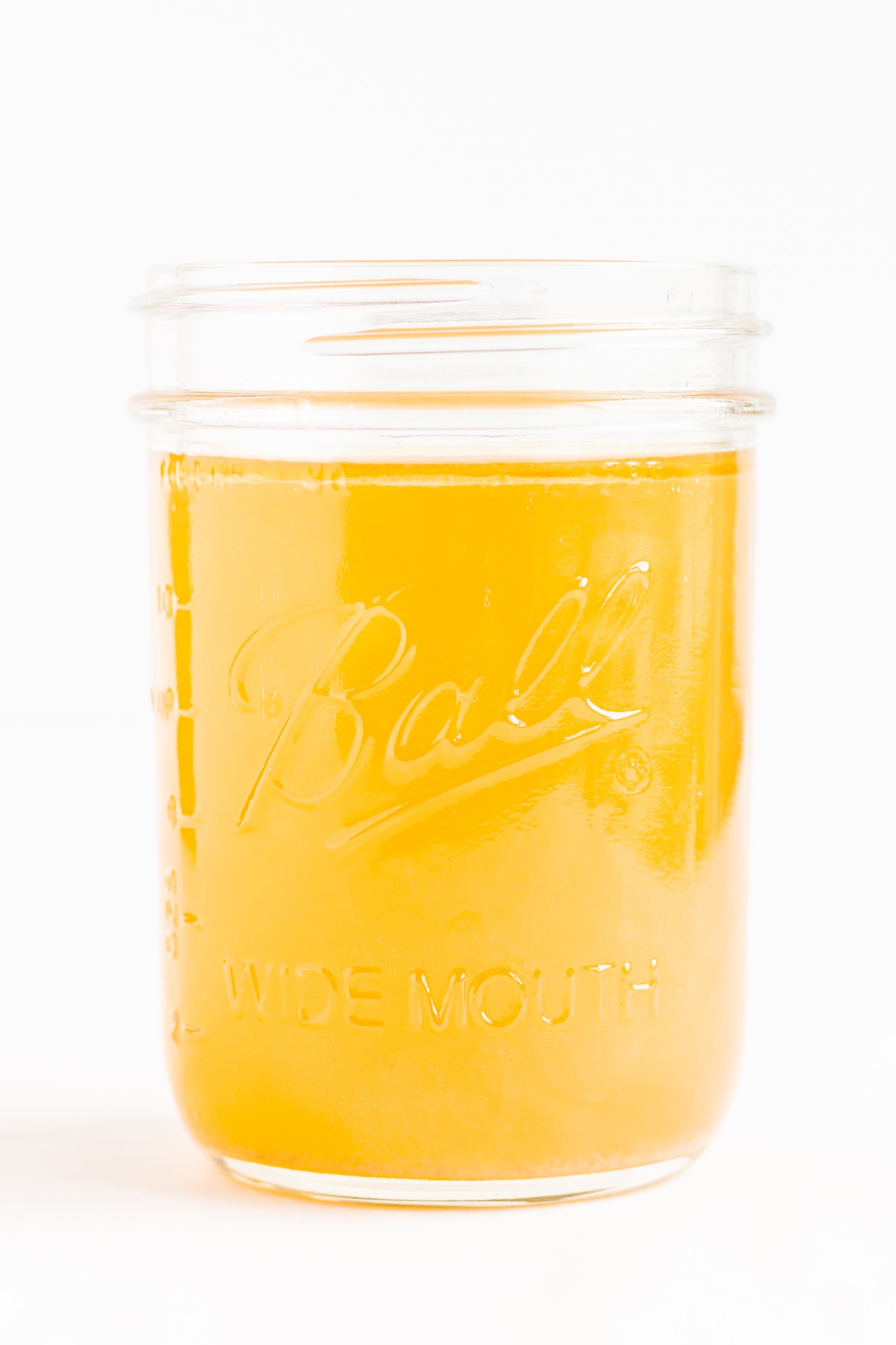 Mason jar filled with chicken bone broth on a white background.