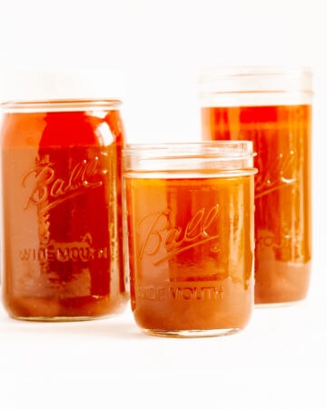 Three different sizes of mason jars filled with beef bone broth (stock) on a white background.