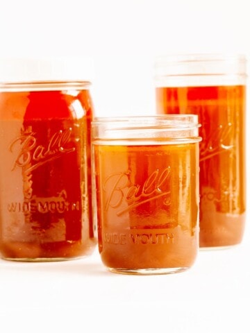Three different sizes of mason jars filled with beef bone broth (stock) on a white background.