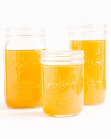 Three mason jars of chicken bone broth (stock) on a white background.