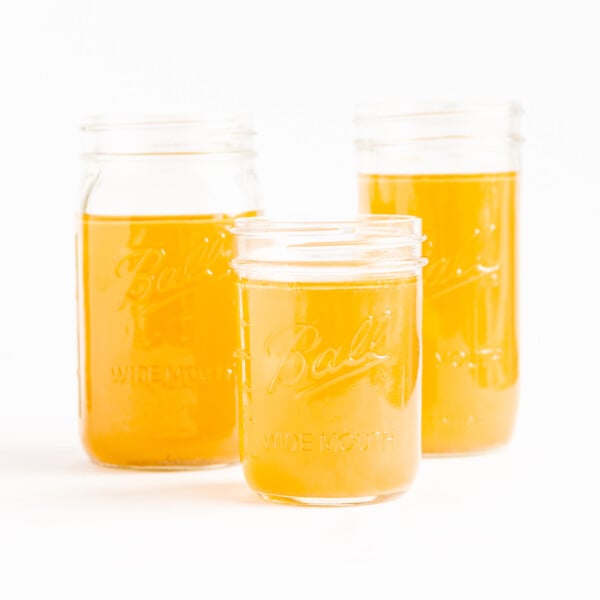 Three mason jars of chicken bone broth (stock) on a white background.