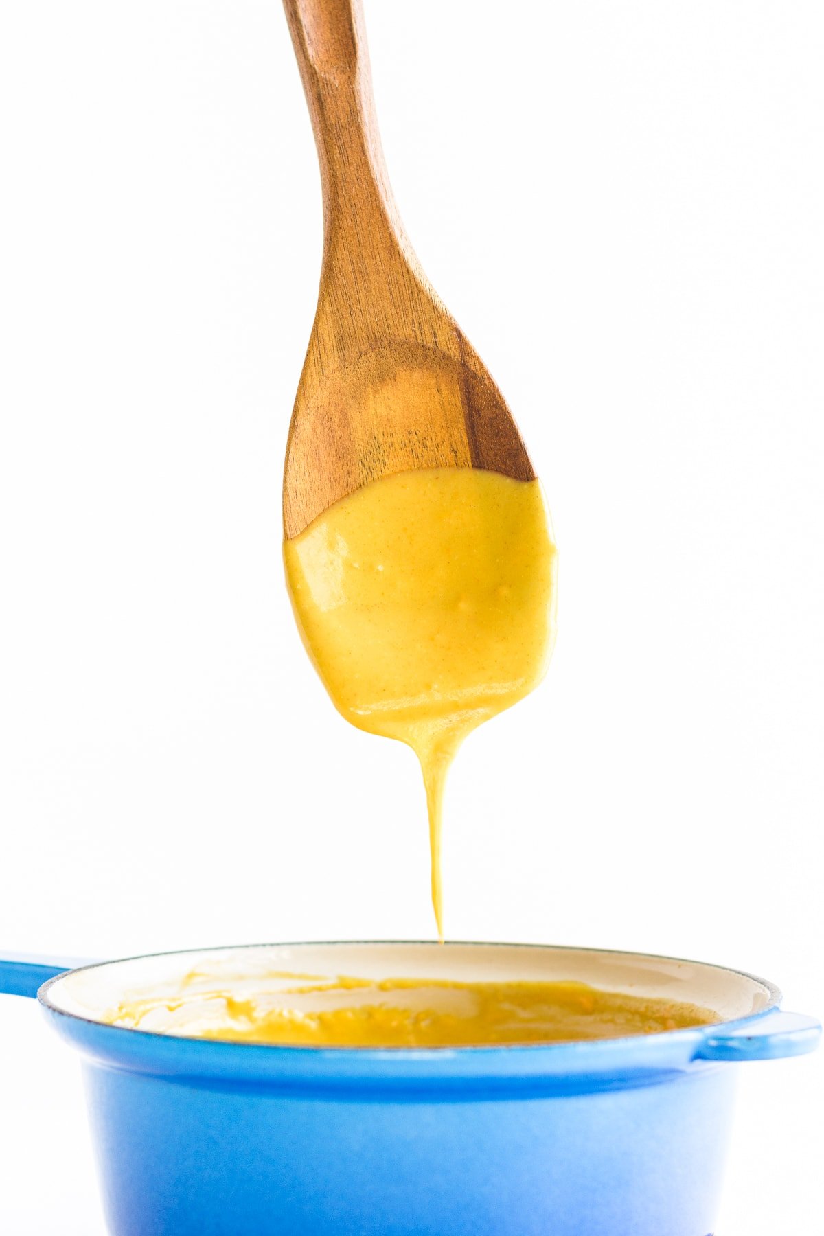 Nacho cheese sauce dripping off a wooden spoon into a blue sauce pan.