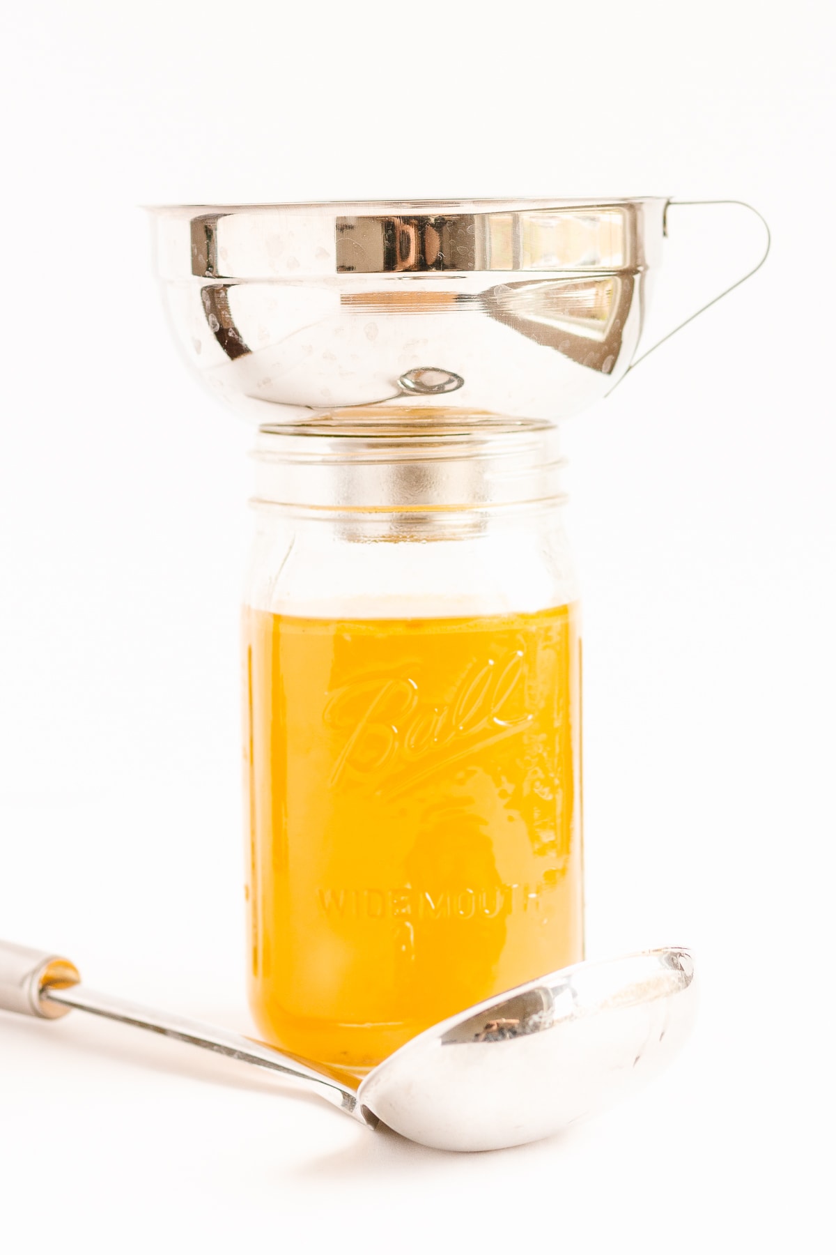 Wide mouth funnel set on top of mason jar filled with broth and ladle lying in front.