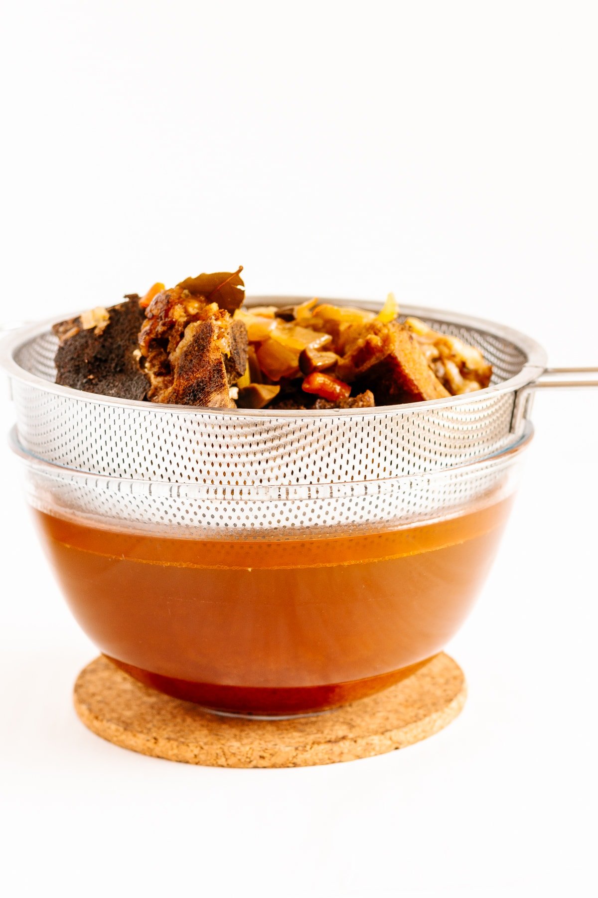 Fine mesh sieve set over a bowl of strained beef broth.