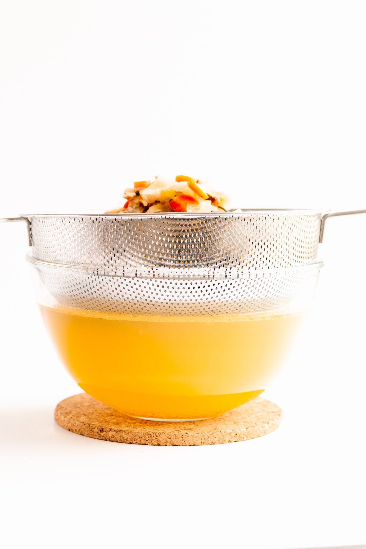 Fine mesh sieve positioned over clear glass bowl straining chicken broth.