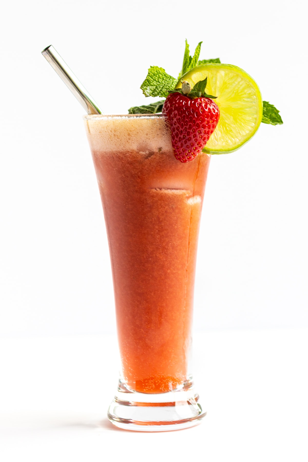 Single glass containing strawberry mojito mocktail and garnished with strawberry, lime, mint and a stainless steel straw.