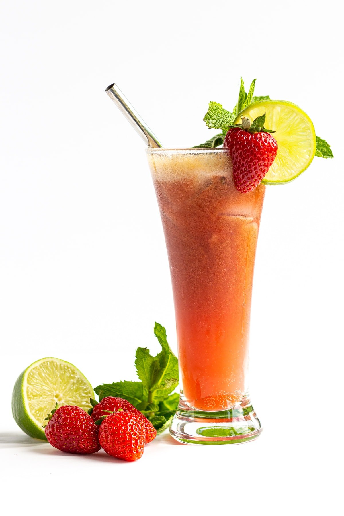 Glass of Strawberry Mojito Mocktail with strawberries, lime and mint sitting next to it.