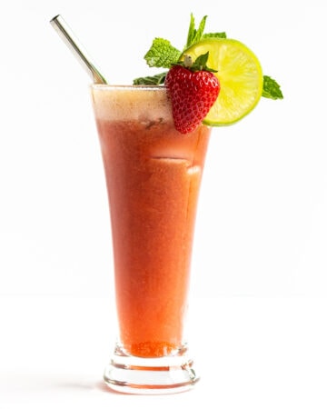 Single glass of Strawberry Mojito Mocktail garnished with a strawberry, lime slice, sprig of mint and stainless steel straw.