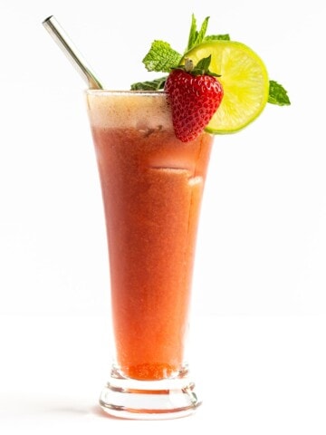 Single glass of Strawberry Mojito Mocktail garnished with a strawberry, lime slice, sprig of mint and stainless steel straw.