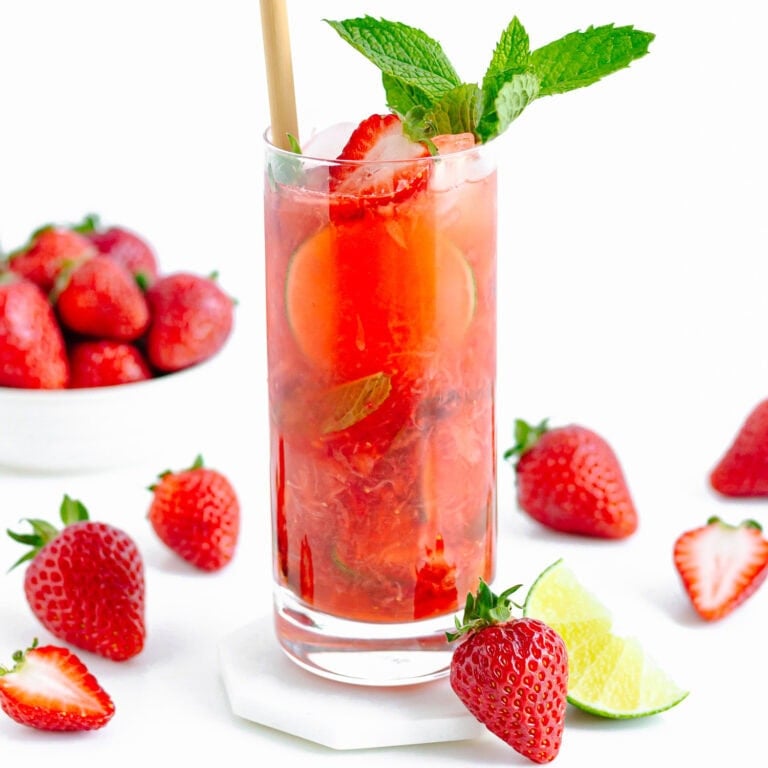 A strawberry mojito mocktail in a tall glass surrounded by strawberries and a lime wedge.