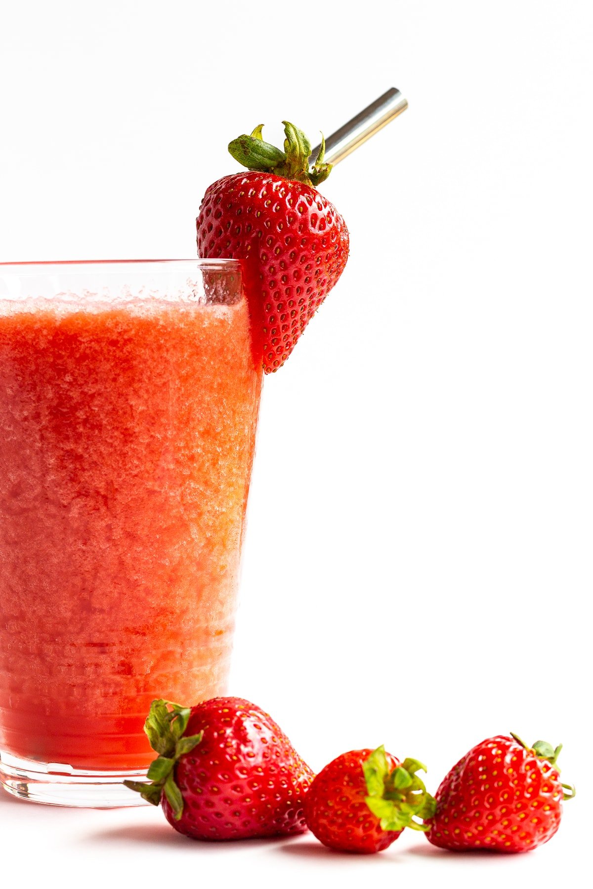 Glass of strawberry slushie with fresh strawberries scattered next to it.