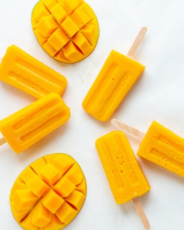 Overhead photo of mango popsicles and fresh mango halves on a white background.