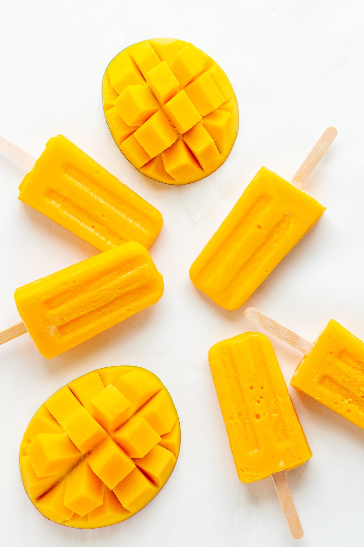 Mango popsicles and fresh mango halves on a white background.