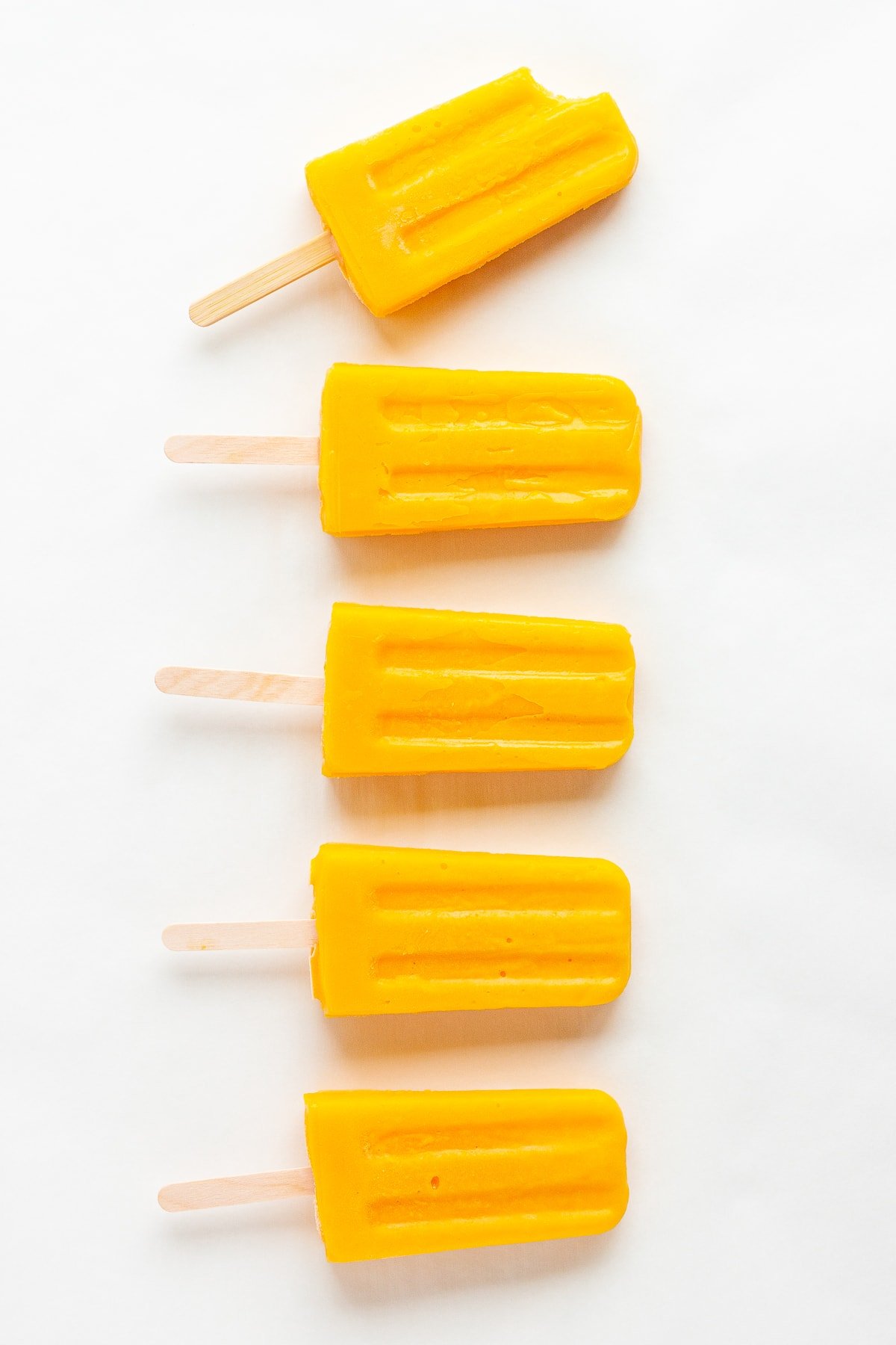 Vertical row of mango popsicles on a white background.