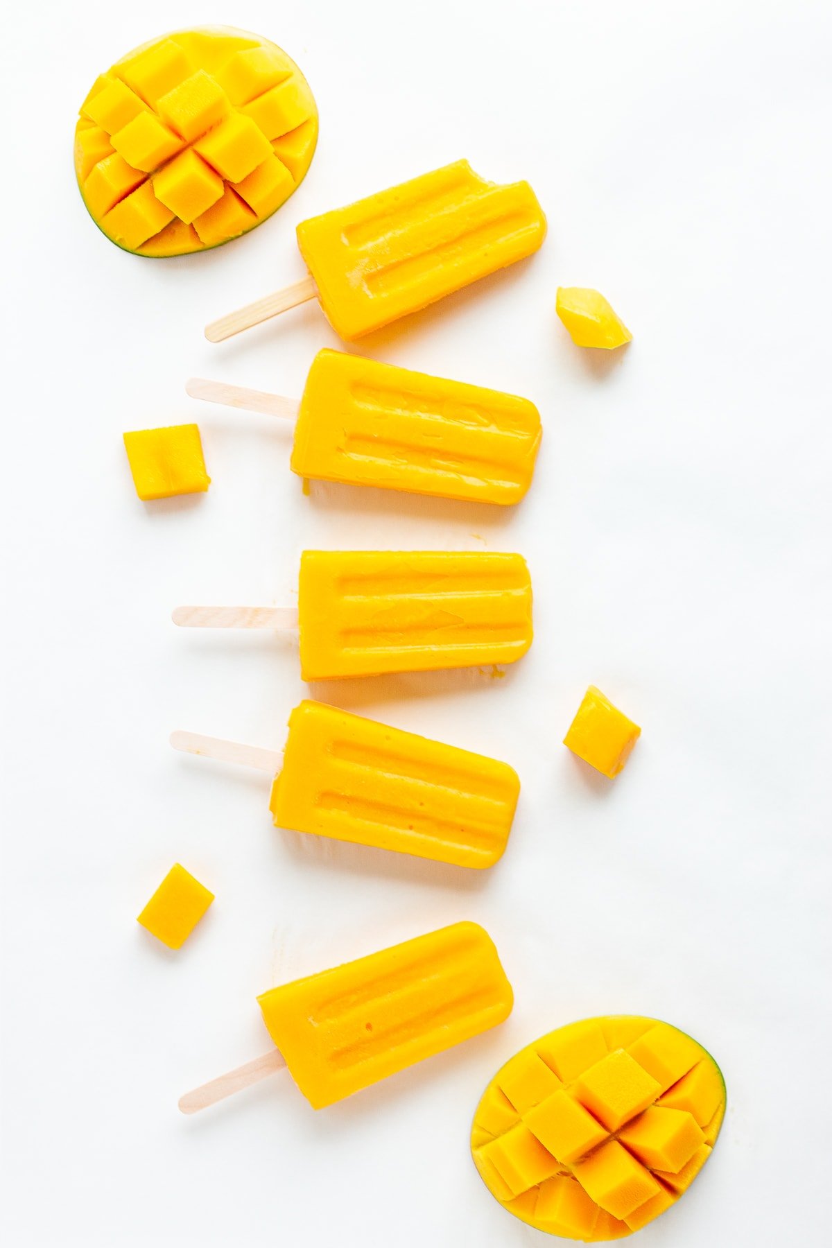 Mango popsicles and fresh mango displayed on a white background.