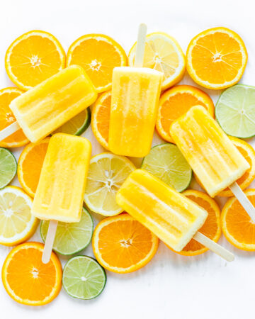 Overhead shot of five orange coloured popsicles displayed on top of orange, lemon and lime slices.